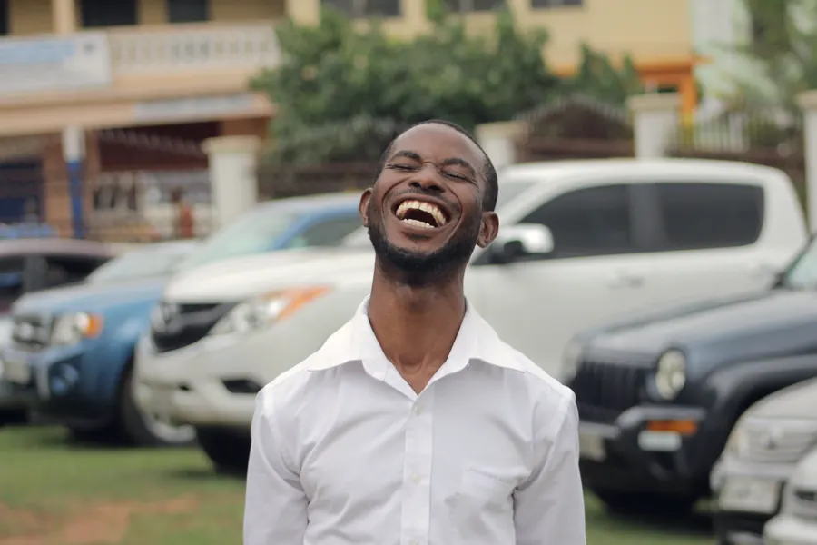 A smiling man in a white shirt standing in front of parked cars