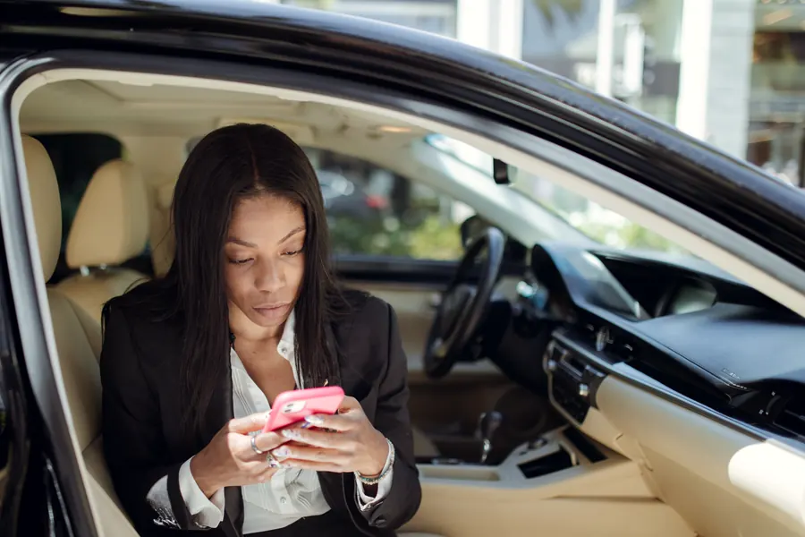 A businesswoman in a suit checking her phone in the driver's seat of her car
